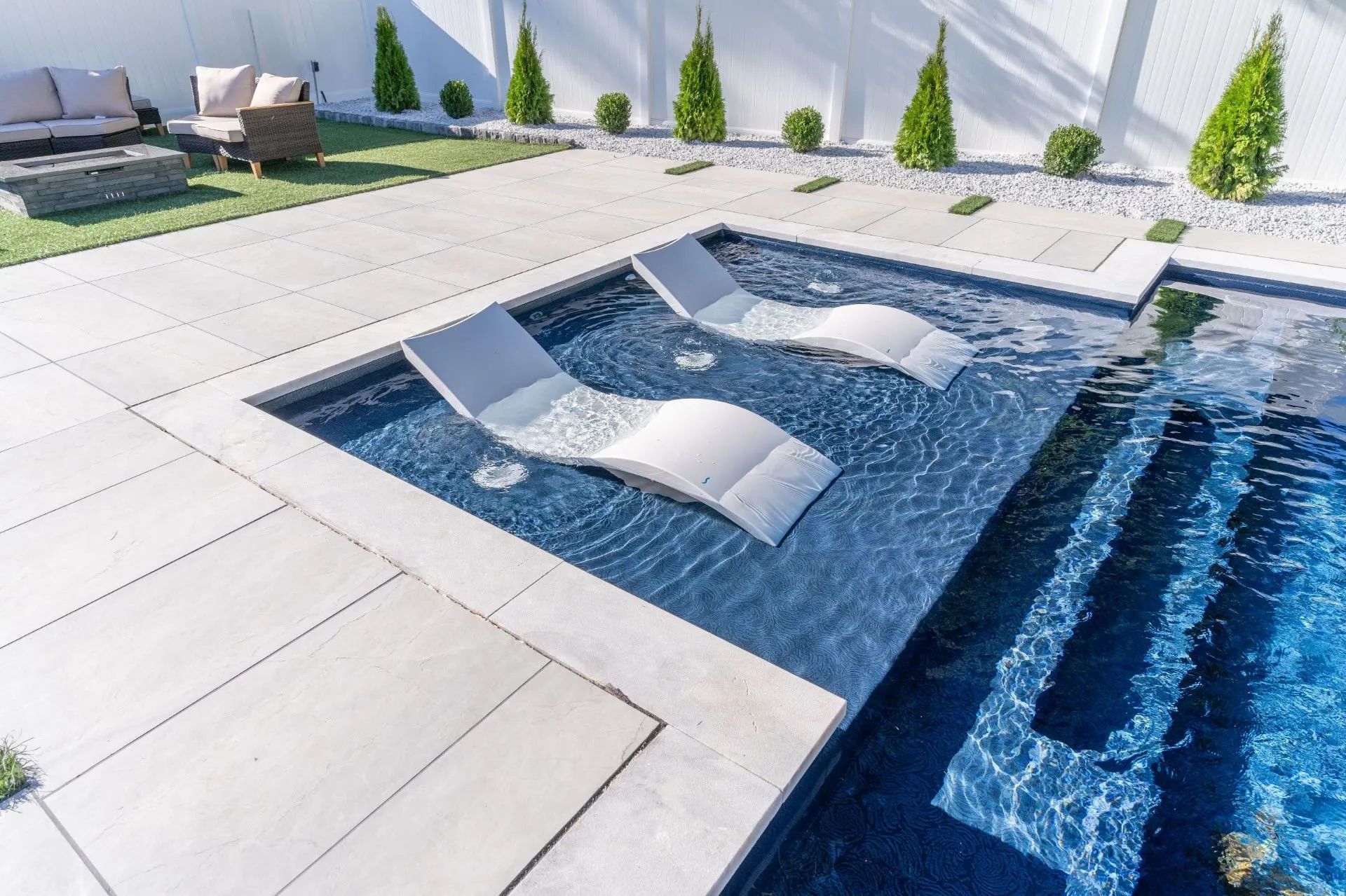 Modern backyard pool with white lounge chairs and blue water beside a tiled deck