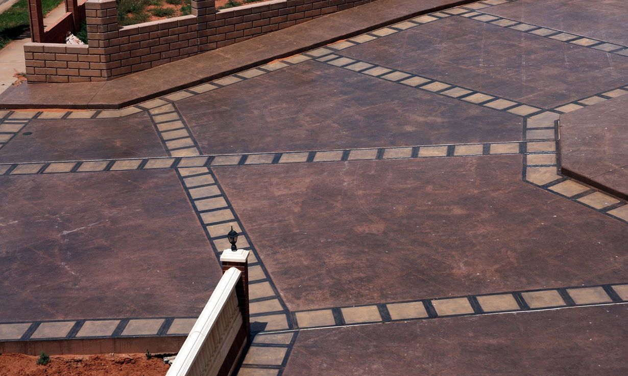 A patio area featuring brown, textured concrete tiles separated by grid-like rows of dark, square paving stones.