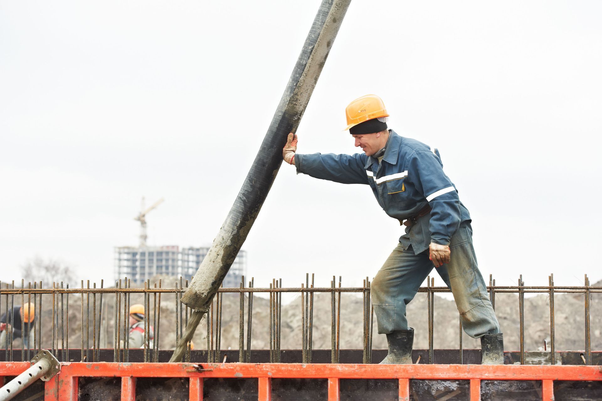 A construction worker in a hard hat guides a concrete delivery hose into metal forms on a building site.