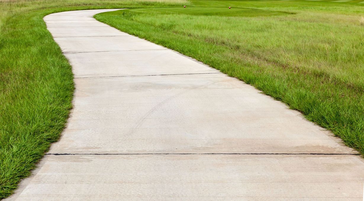 A curved concrete sidewalk flanked by green grass under natural light.