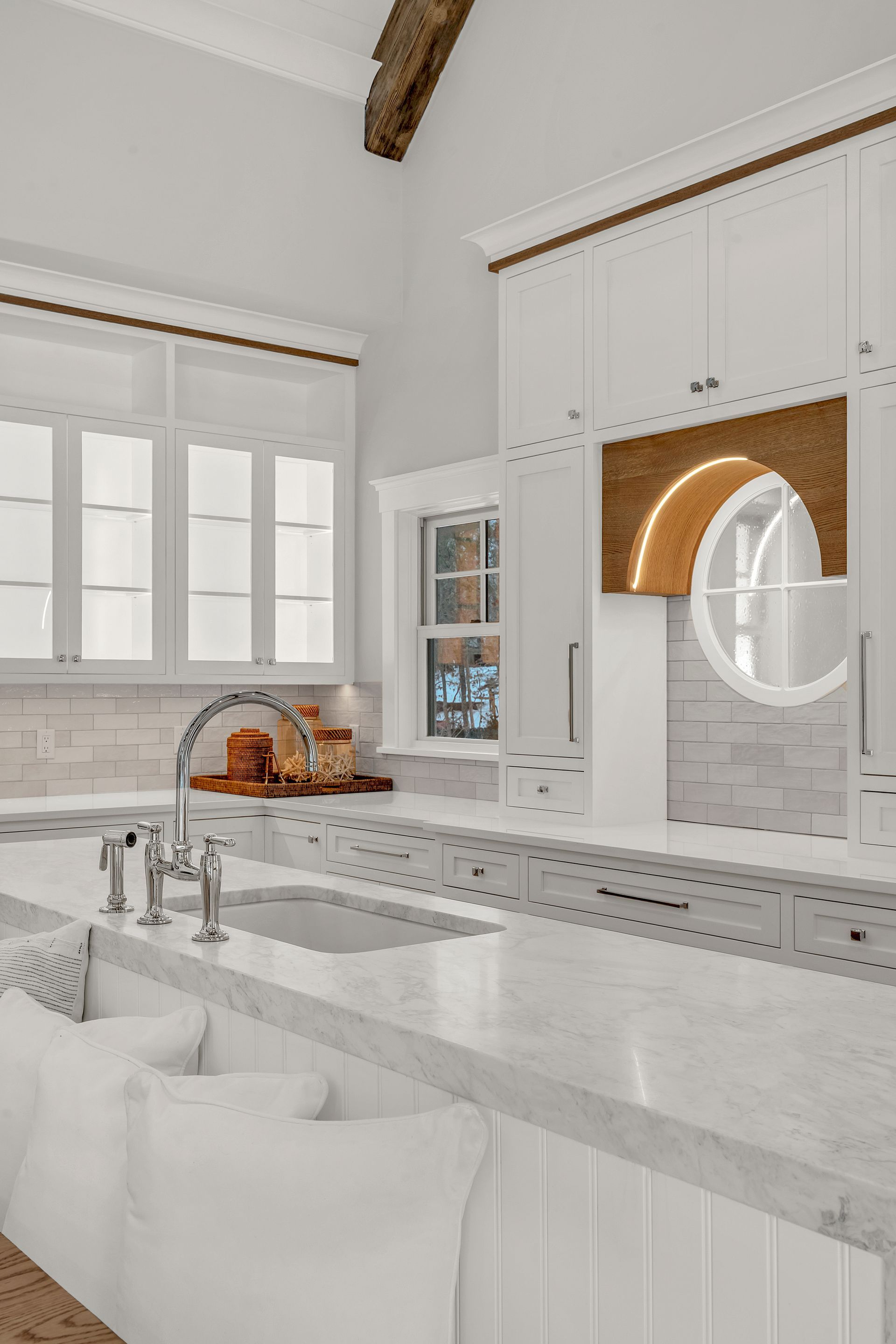 Bright kitchen island with white counters, stools, and cabinetry featuring a warm wood arched hood over the stove area.