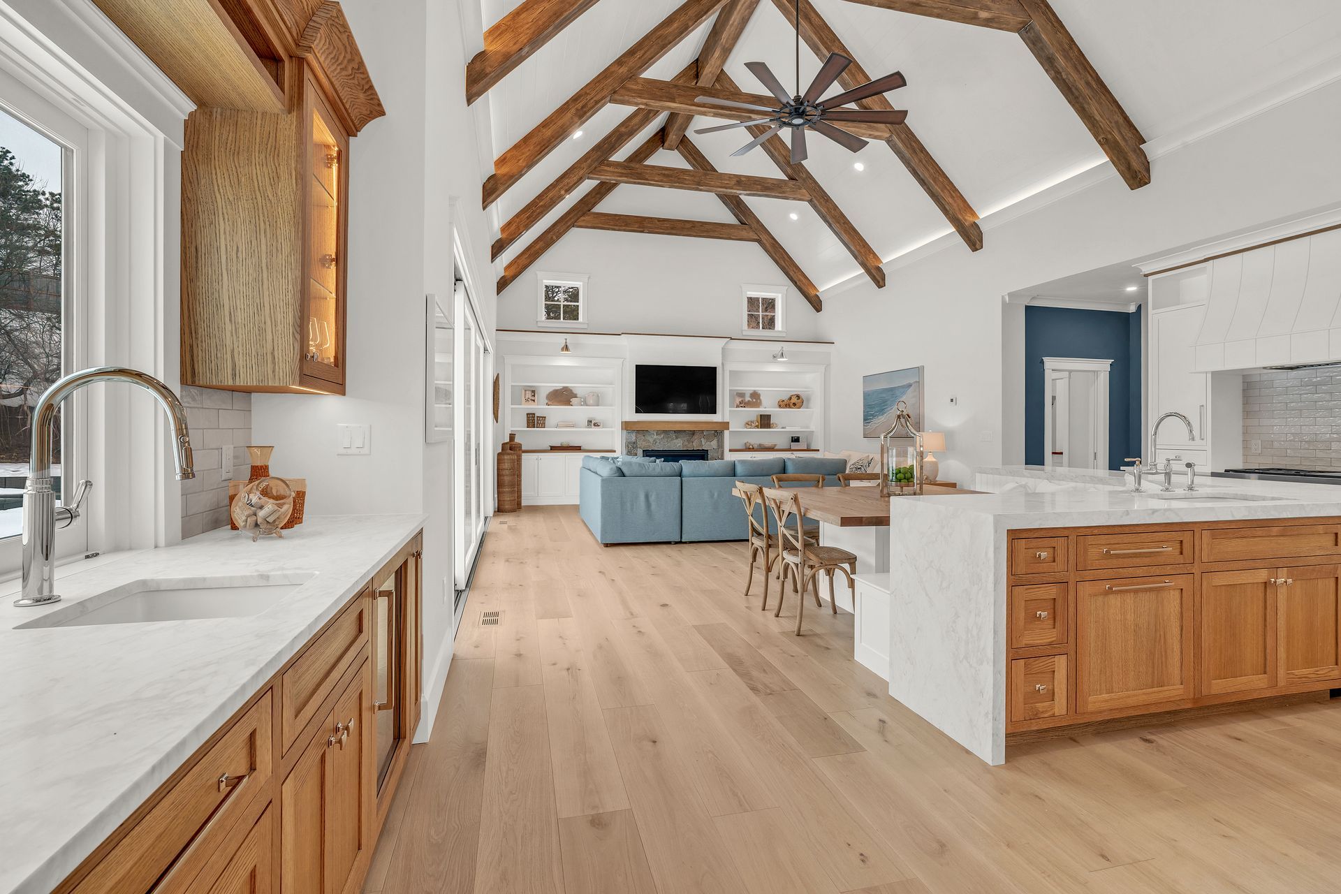An open-concept kitchen and living area with wood vaulted ceilings, light wood floors, and warm-toned wooden cabinets.