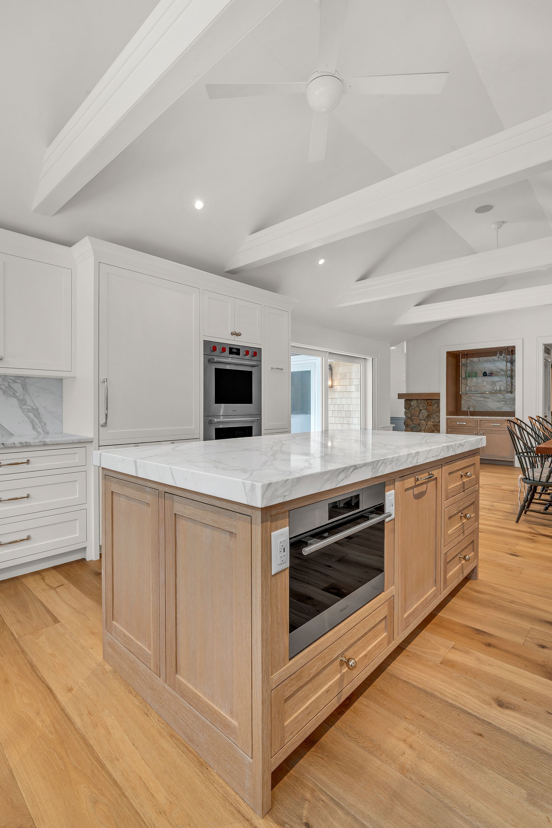 A bright kitchen with a light wood island, marble countertops, white cabinets, vaulted ceilings, and light wood flooring.