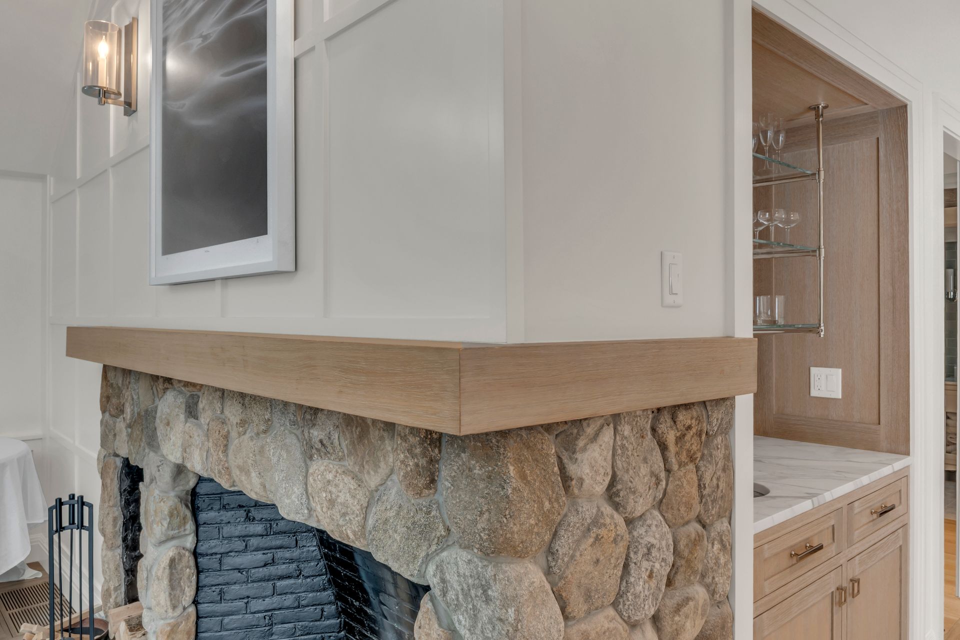 A stone fireplace with a natural wood mantel sits next to a small, built-in bar with glass shelving and marble counters.