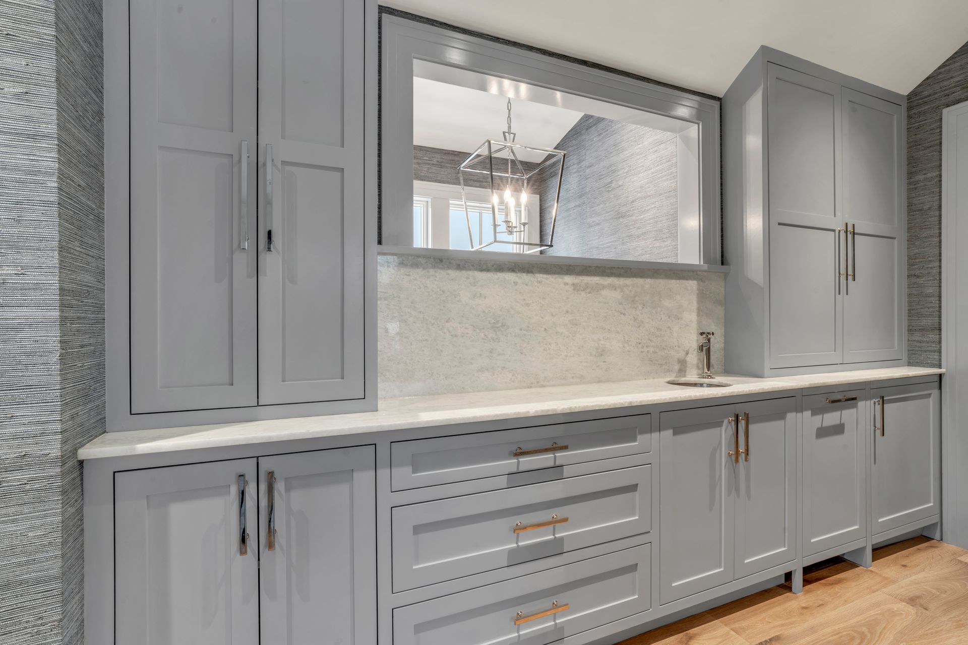 Modern light gray cabinets and drawers with brushed gold hardware, marble countertop, and a mirror in a laundry room.