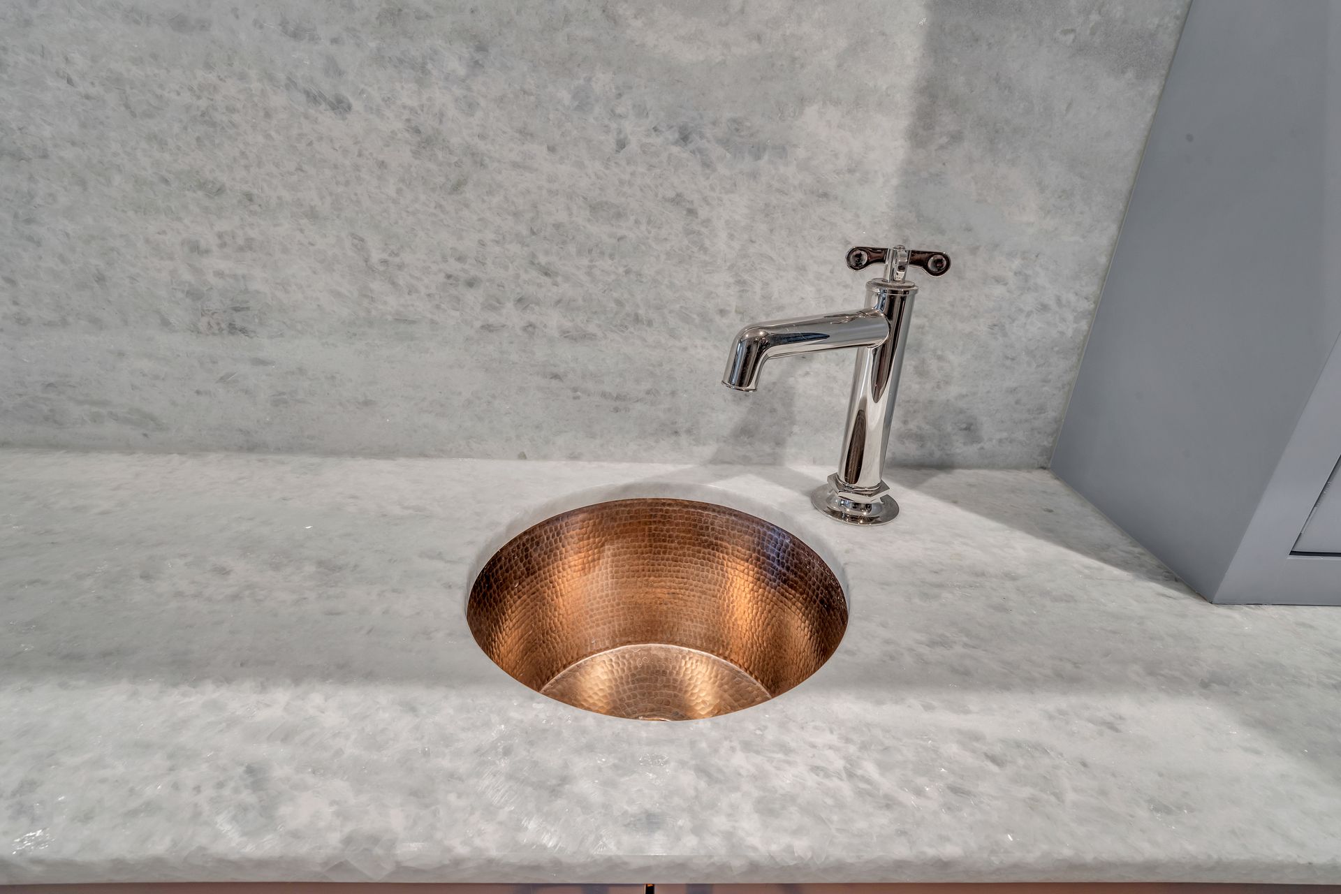 A polished copper sink set into a white marble countertop with a silver faucet.