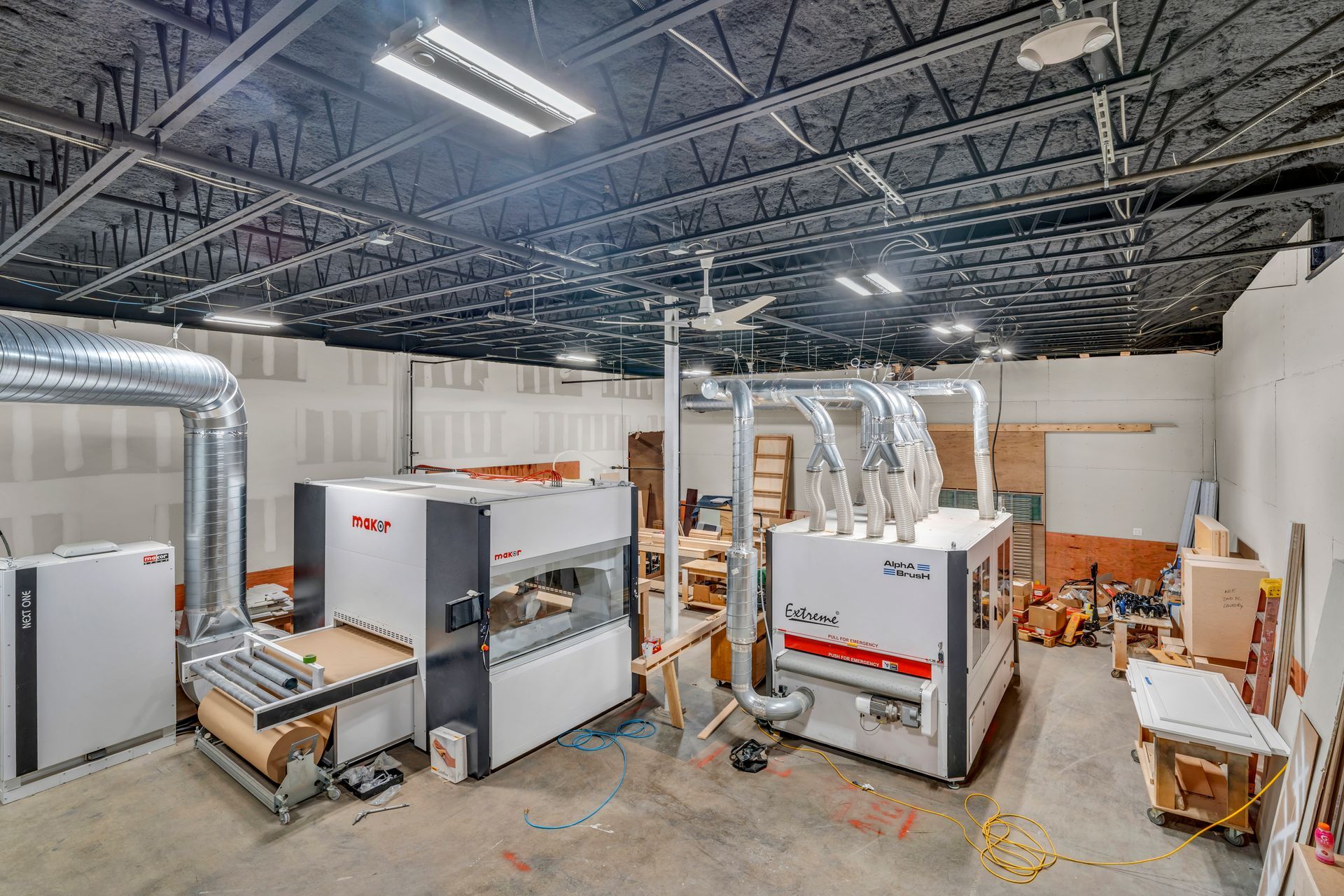 Two large, white industrial sanding machines in a spacious workshop with a black, exposed-joist ceiling.