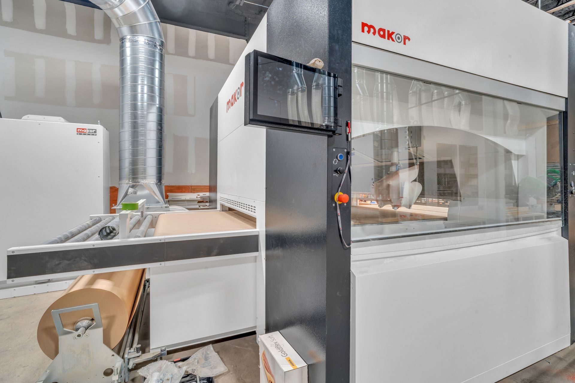 A large white industrial CNC woodworking machine in a factory, featuring a control screen and a roll of raw material.