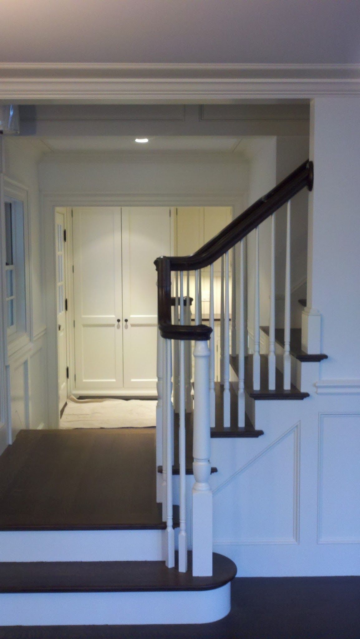 A staircase with dark wooden steps and handrail, featuring white balusters and wainscoting leading to a white doorway.