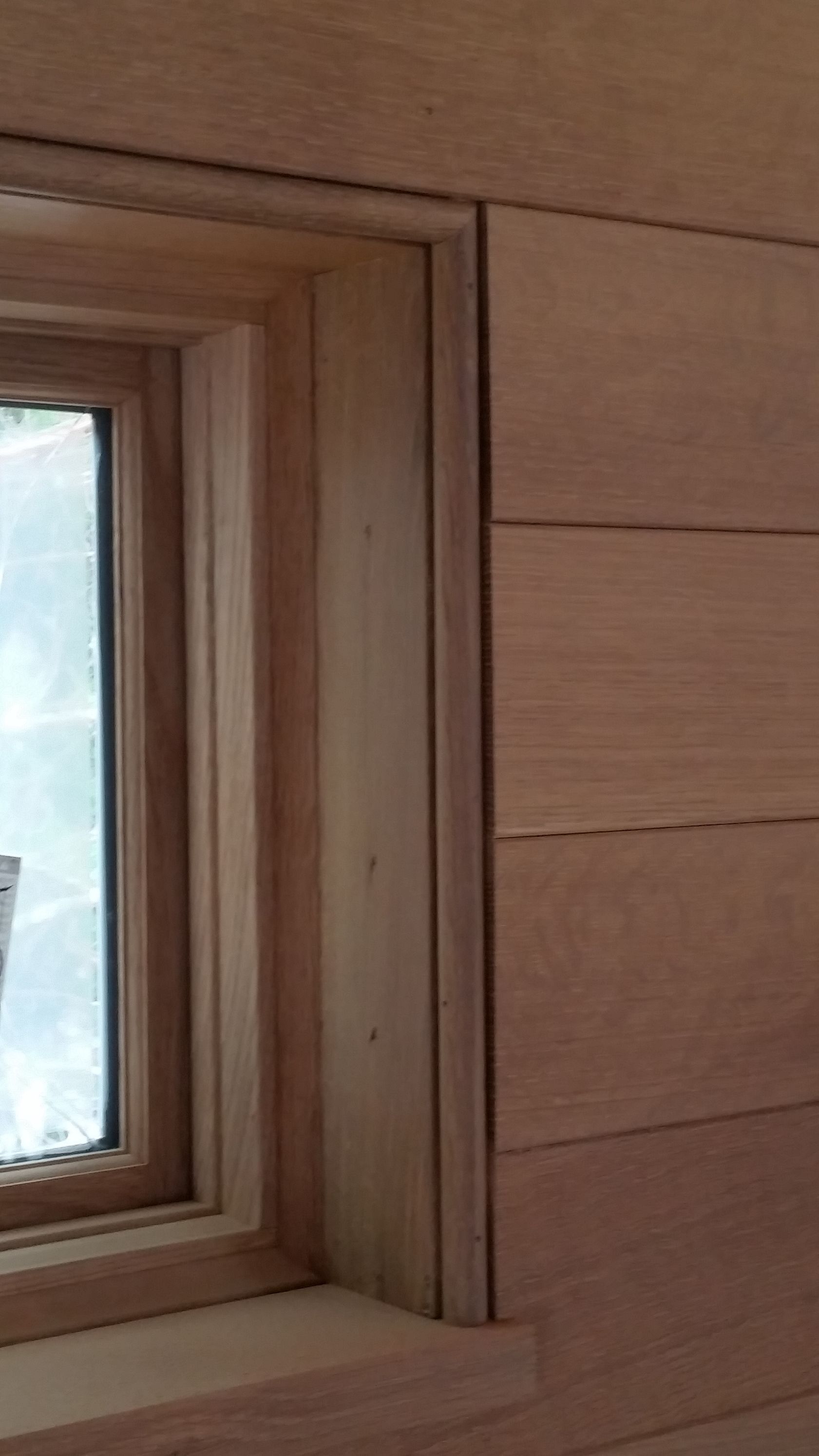 A close-up of a window frame featuring natural-toned wood trim set against horizontal wood paneling.