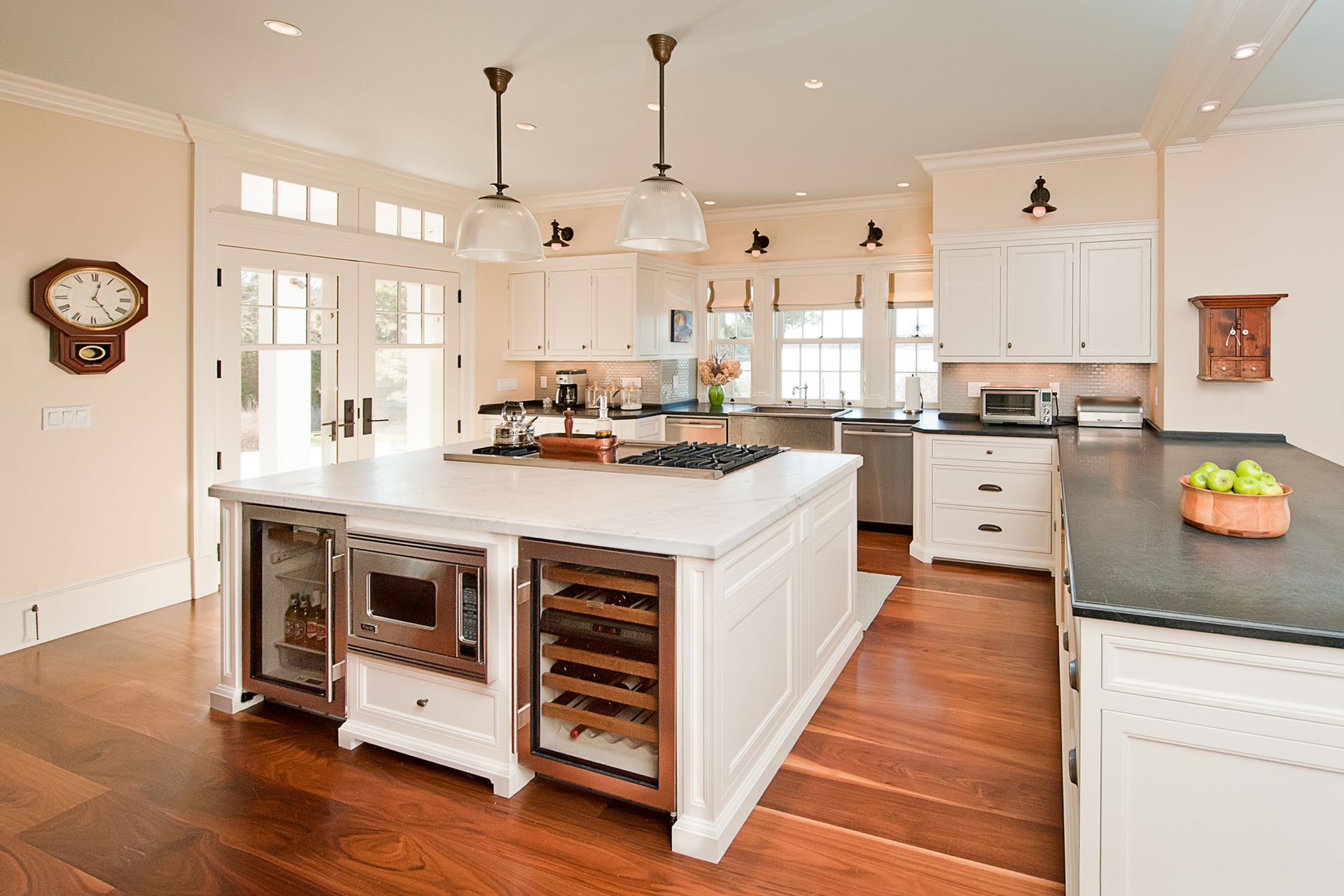 A bright, modern kitchen featuring a large white center island with a wine cooler, microwave, and wood floors.