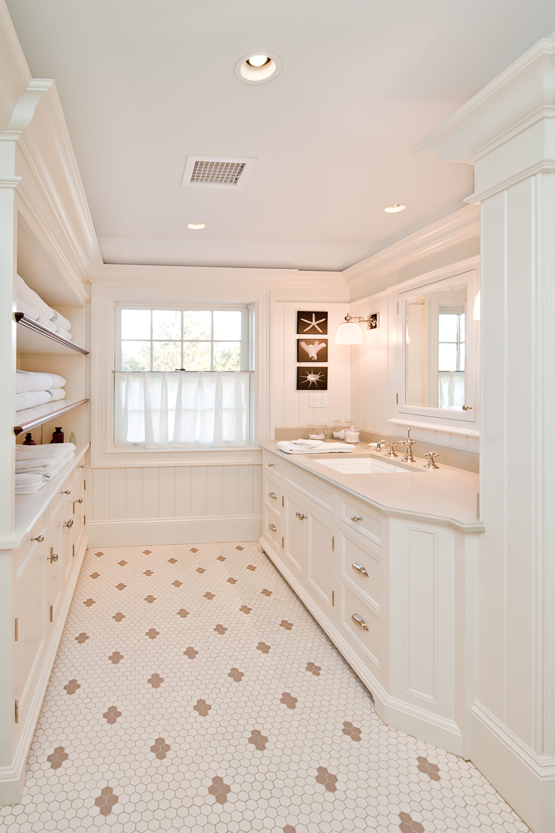 A light-filled bathroom with white cabinetry, a double vanity, patterned tile floors, and open shelving with towels.