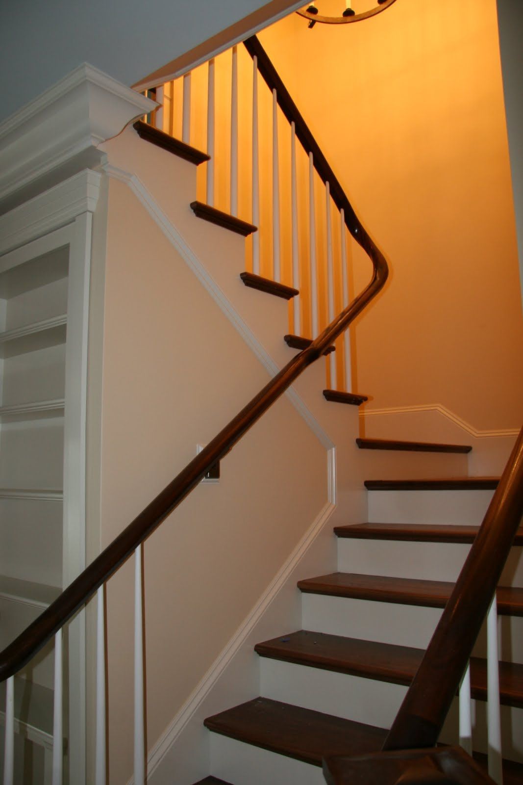 A staircase with dark wood treads and white risers, featuring white balusters and a dark wood handrail, leading upward.