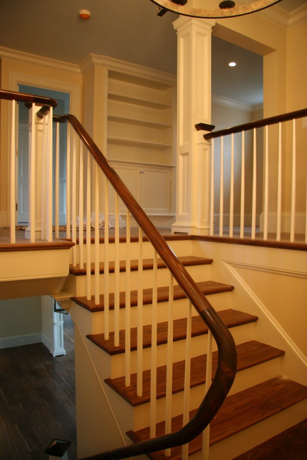 A wood and white staircase with a curved handrail leading to a landing with a built-in bookshelf in a bright hallway.