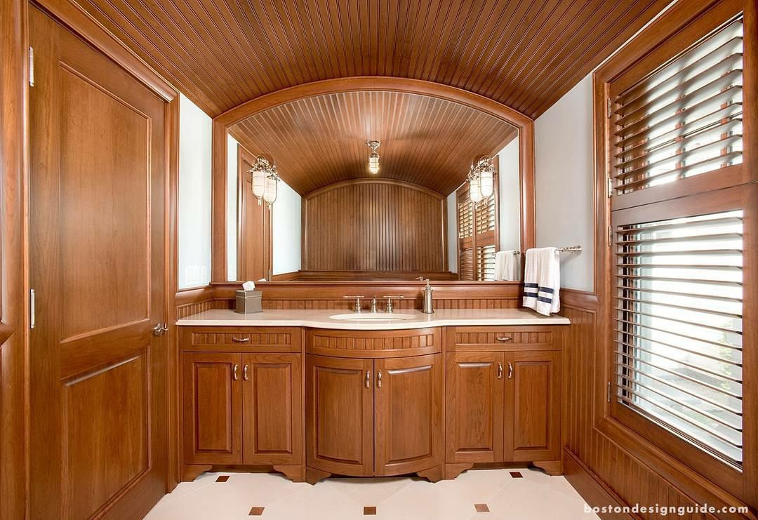 A wooden bathroom vanity with a central sink and large mirror, featuring an arched wood-paneled ceiling and shutter windows.
