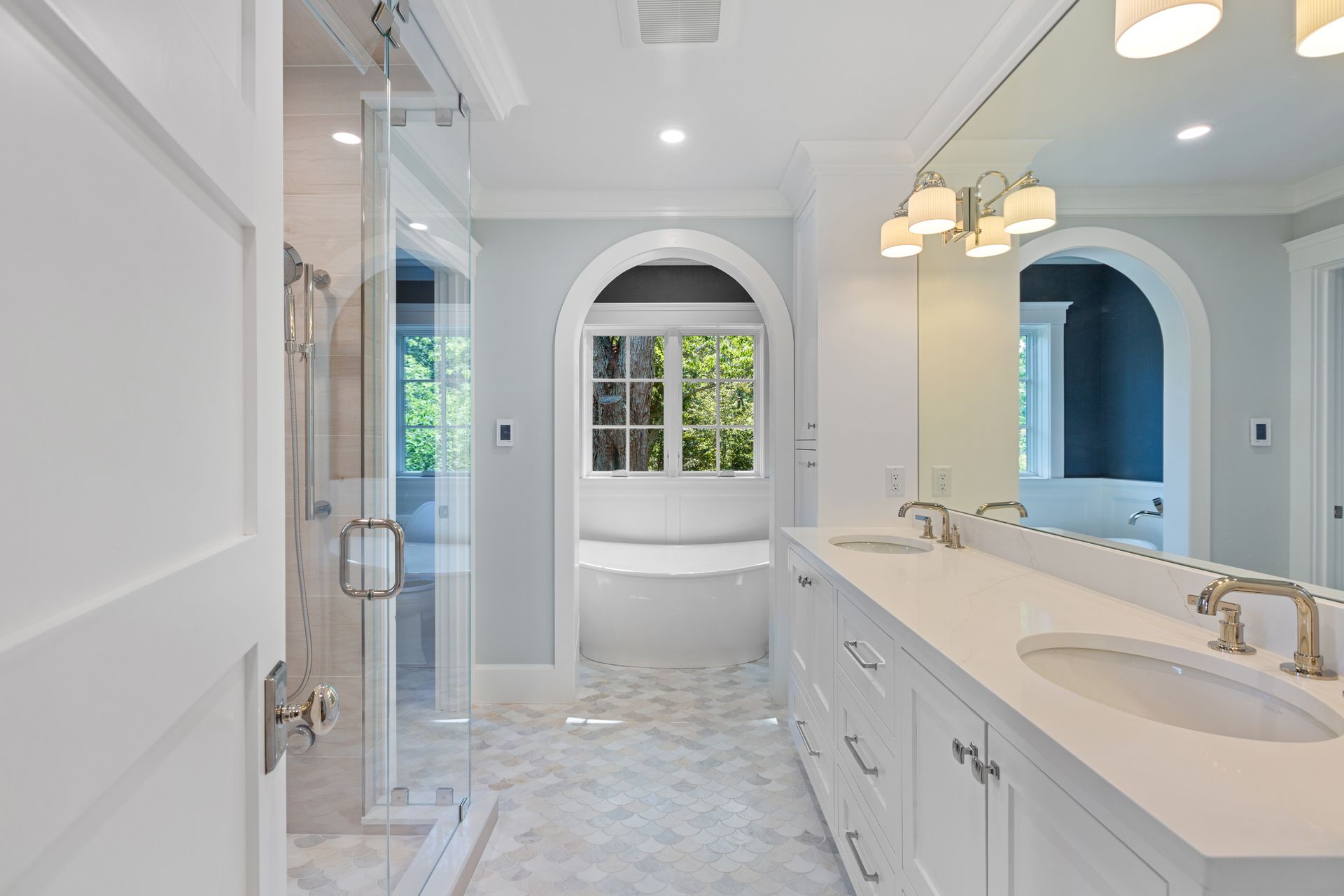 Bright, modern bathroom with a white double vanity, glass-enclosed shower, and a soaking tub in an arched alcove.