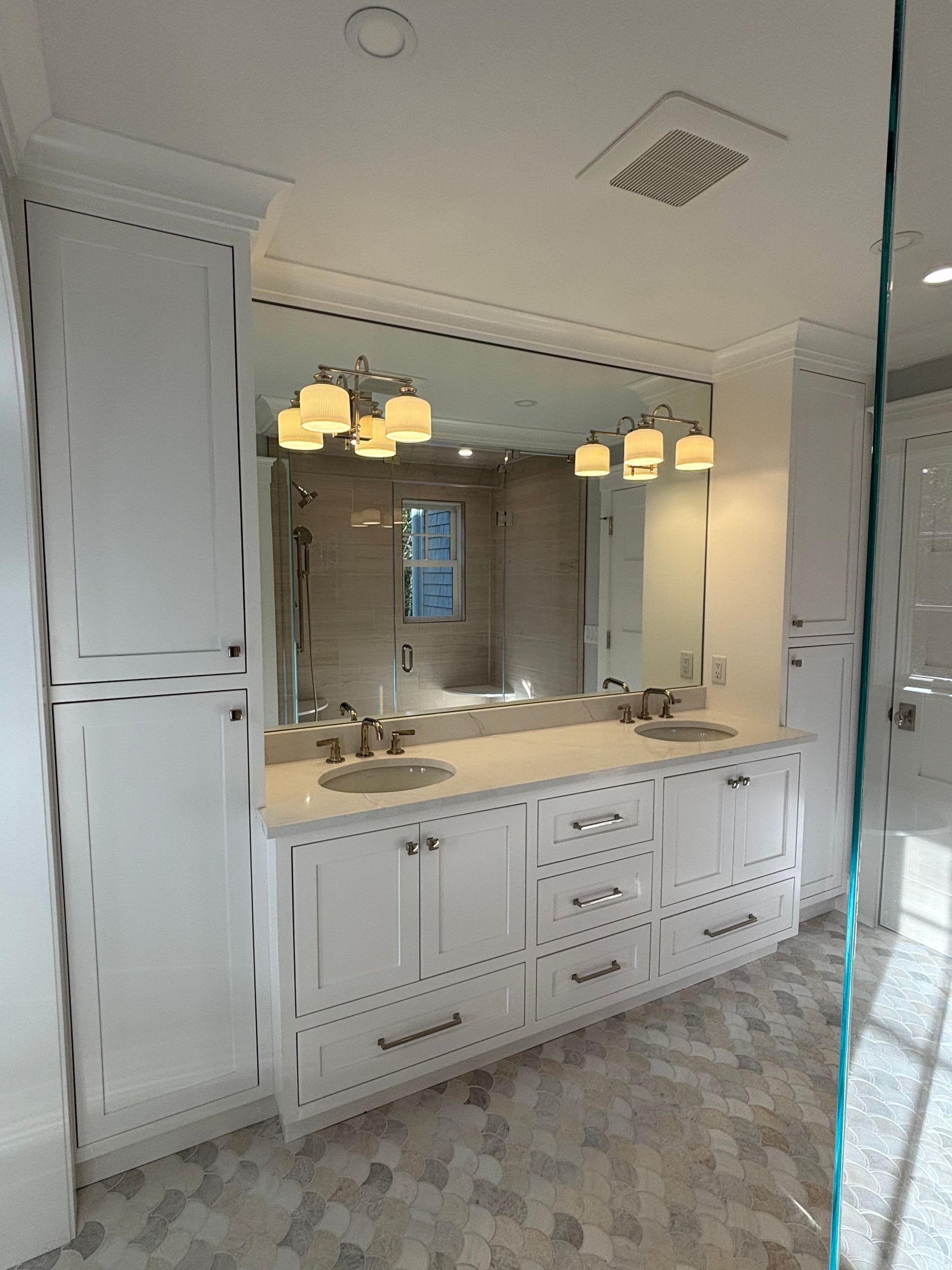 A double bathroom vanity with white cabinets, marble countertops, two sinks, mirrors, and vanity lights.