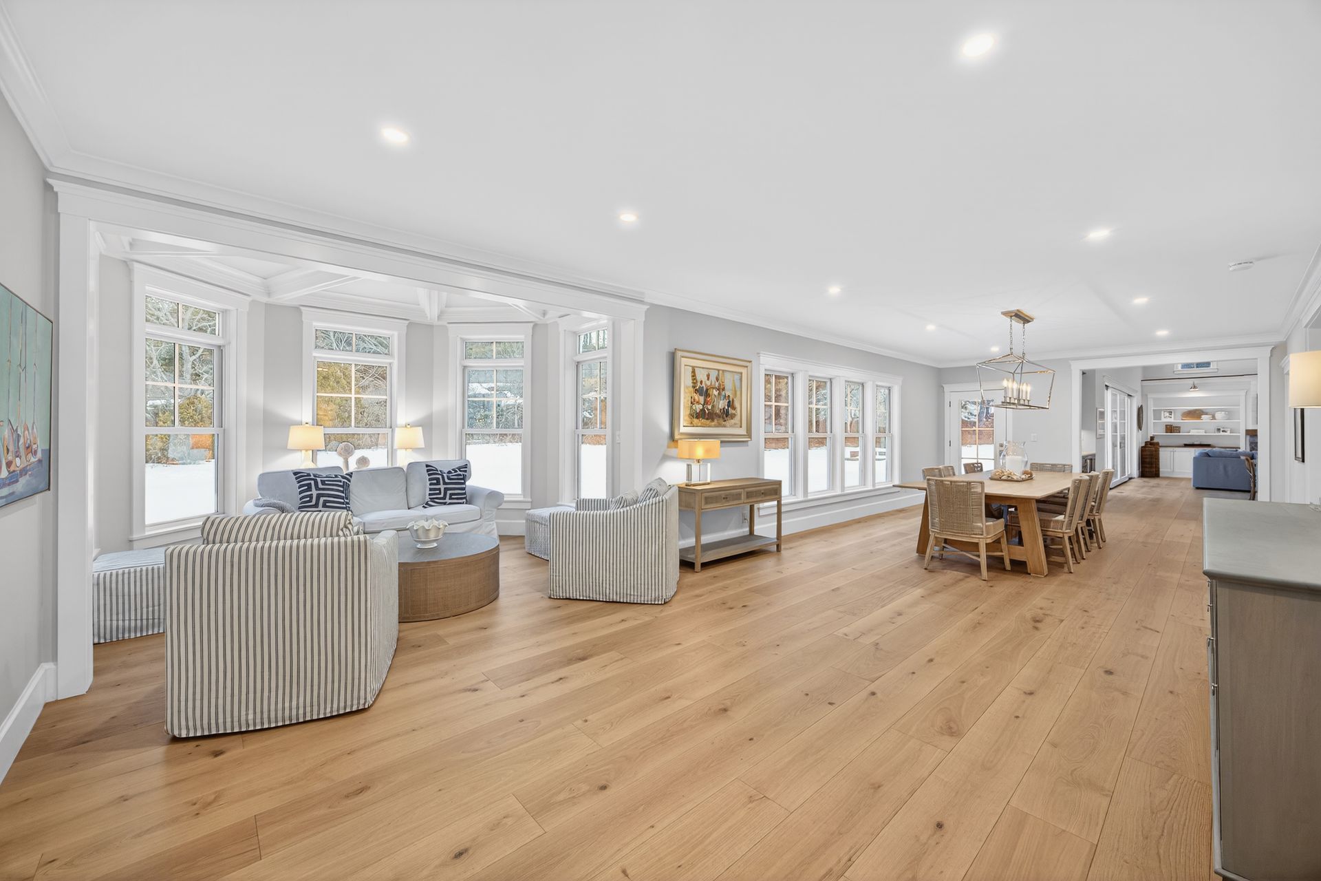 Spacious, bright living area with light wood floors, a dining table, and large windows.