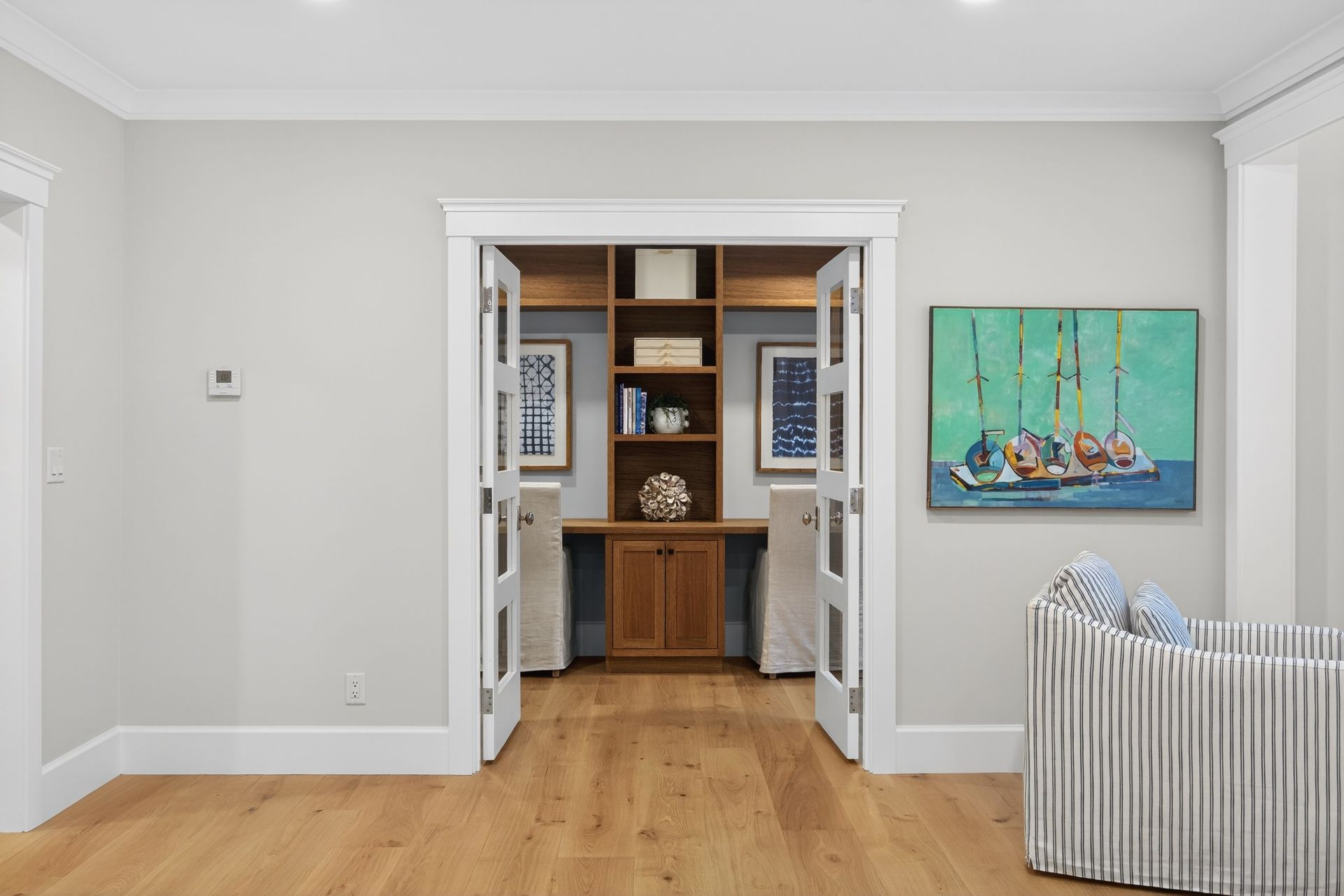 Home office nook with built-in desk, shelving, and double doors.  Artwork and striped chair are visible.