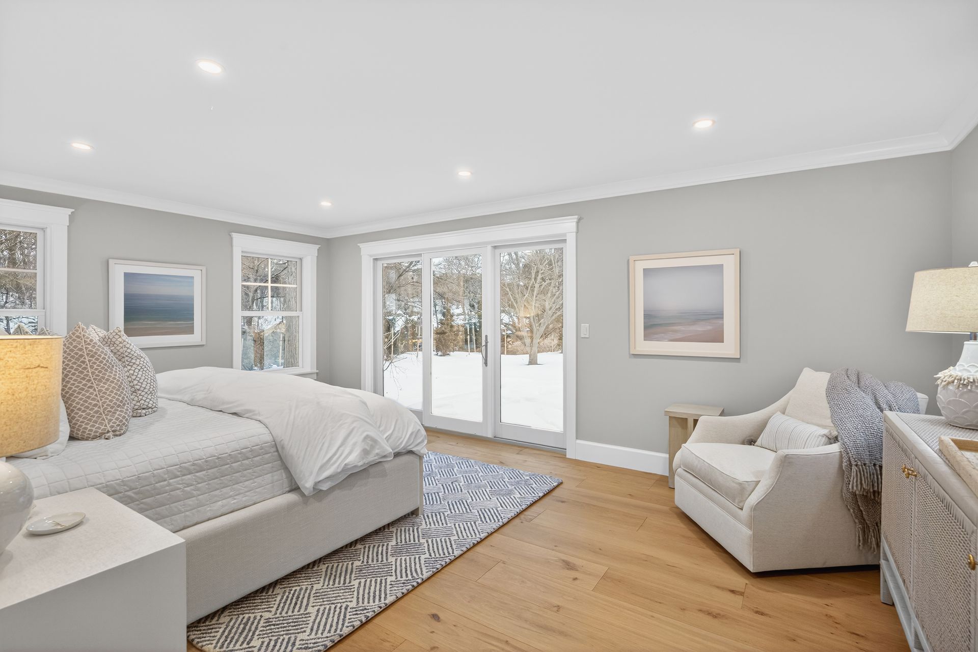 Spacious, light gray bedroom with white trim, light wood floors, and snow-covered view through sliding glass doors.