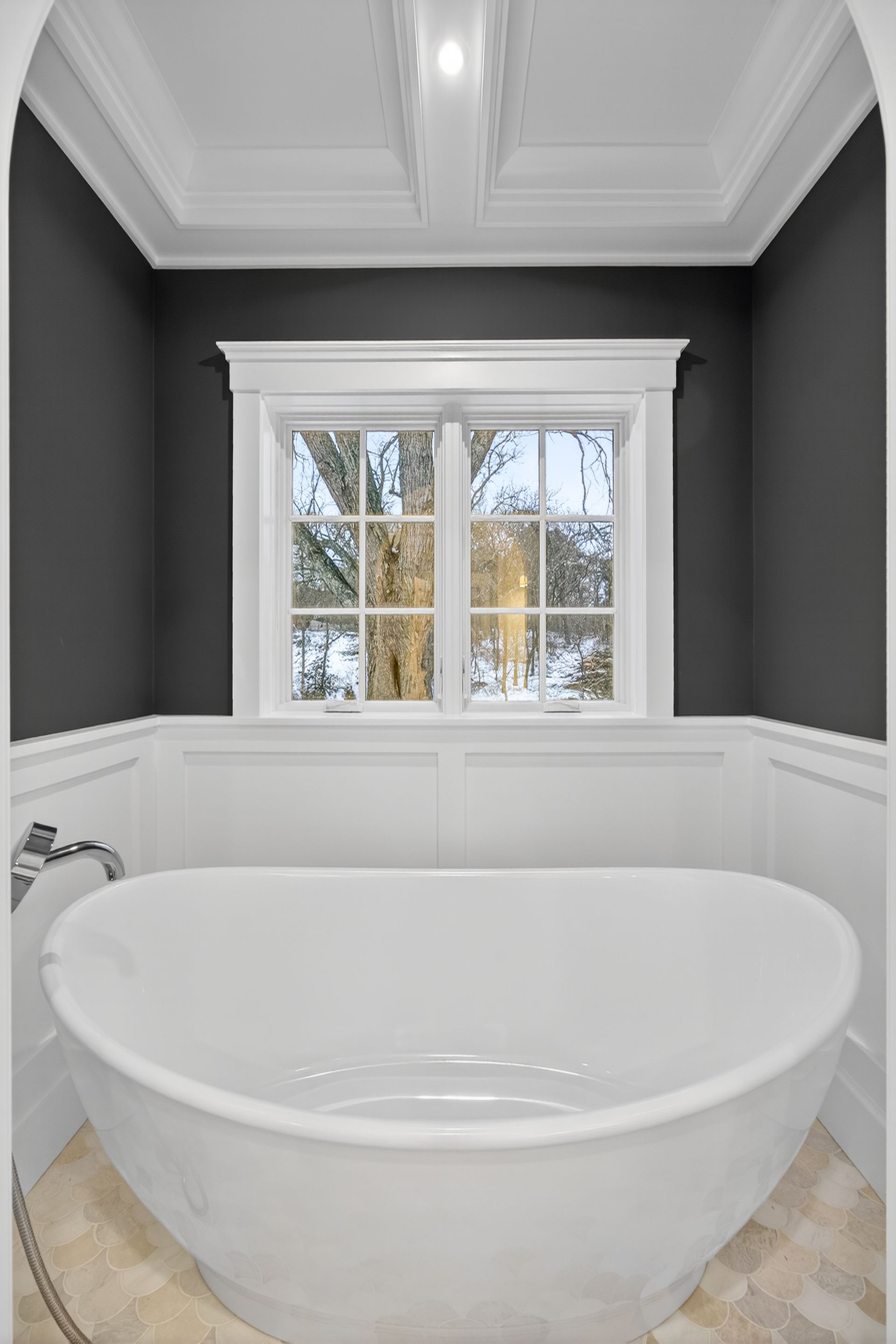 White soaking tub in a bathroom with dark gray walls and a window.