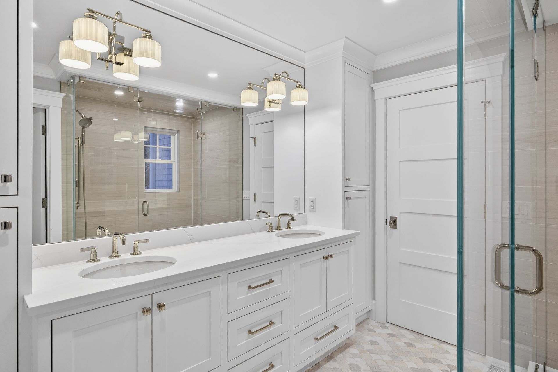 White bathroom with a double vanity, large mirror, glass shower, and white door.