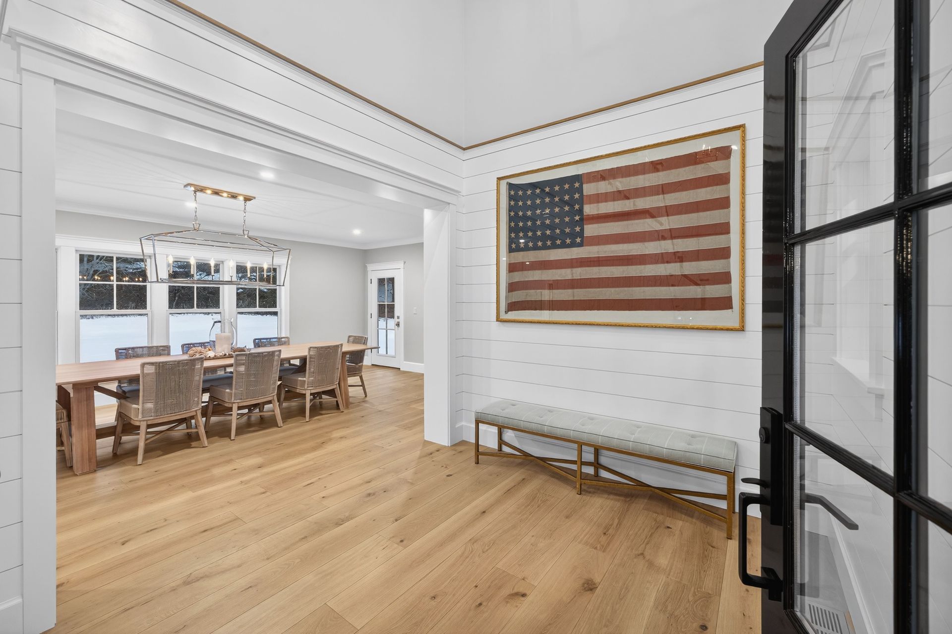 A bright foyer with a wood floor, an American flag, and a dining room visible.