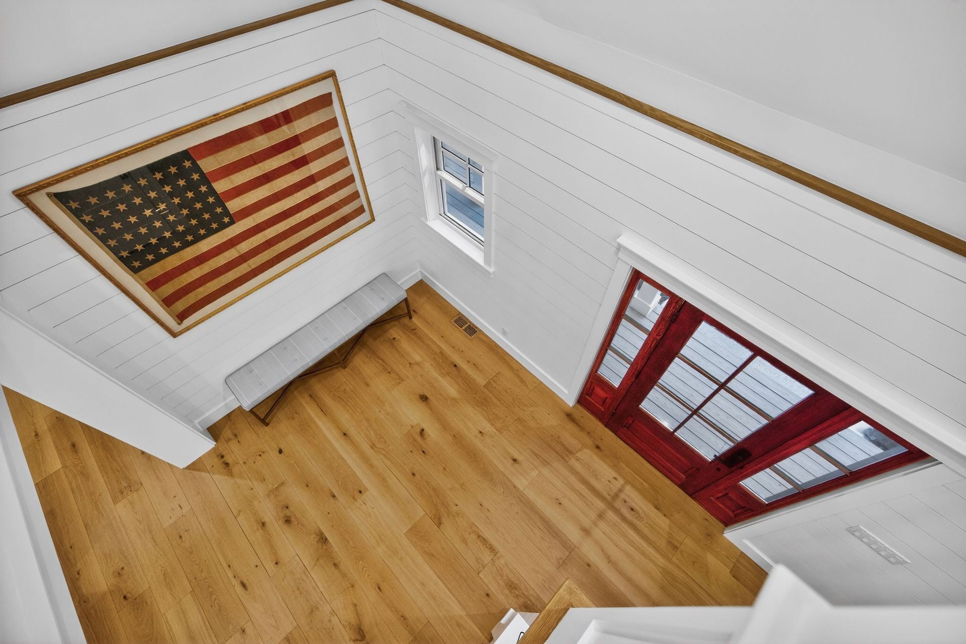 Interior entryway with a red door, American flag, wood floor, and white walls.