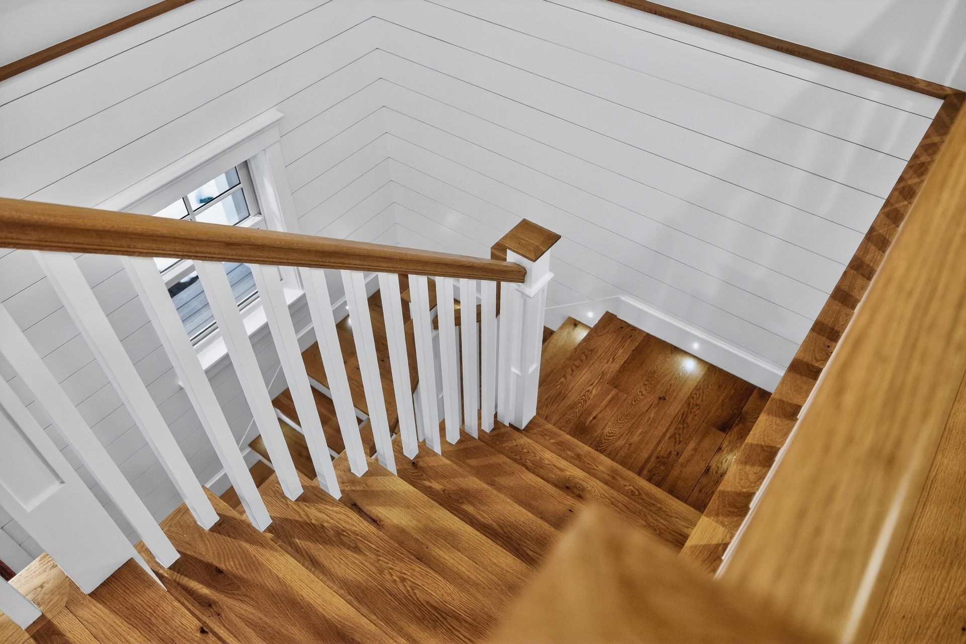 Wooden staircase with white railing, viewed from above.