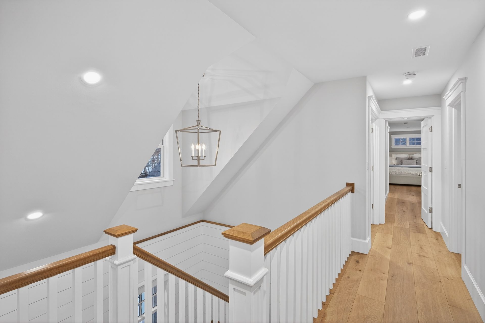Hallway with white walls, wood floors, and a hanging light fixture.