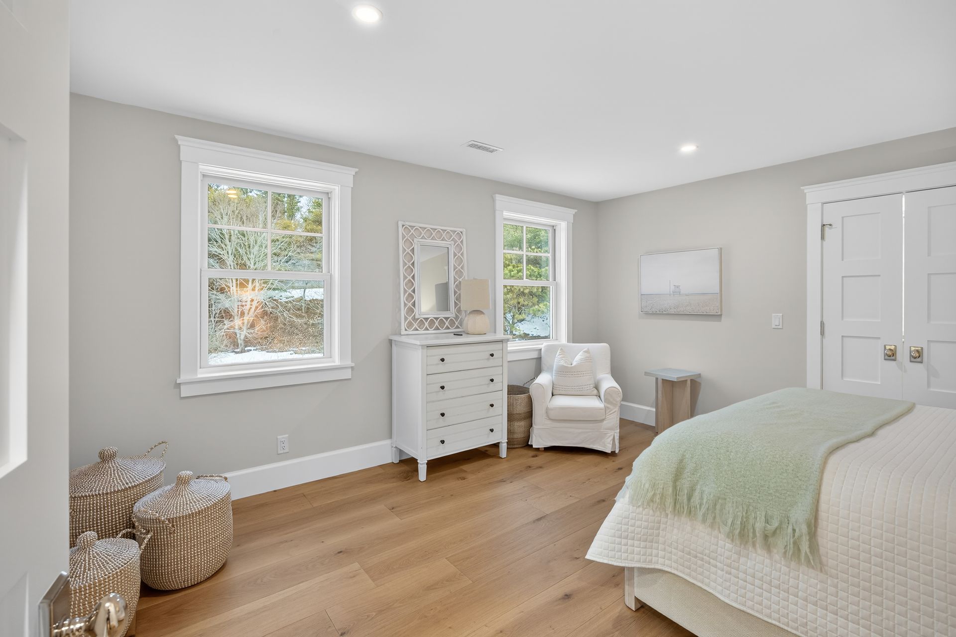 Bedroom with light wood floor, white furniture, two windows, and pale green blanket on bed.