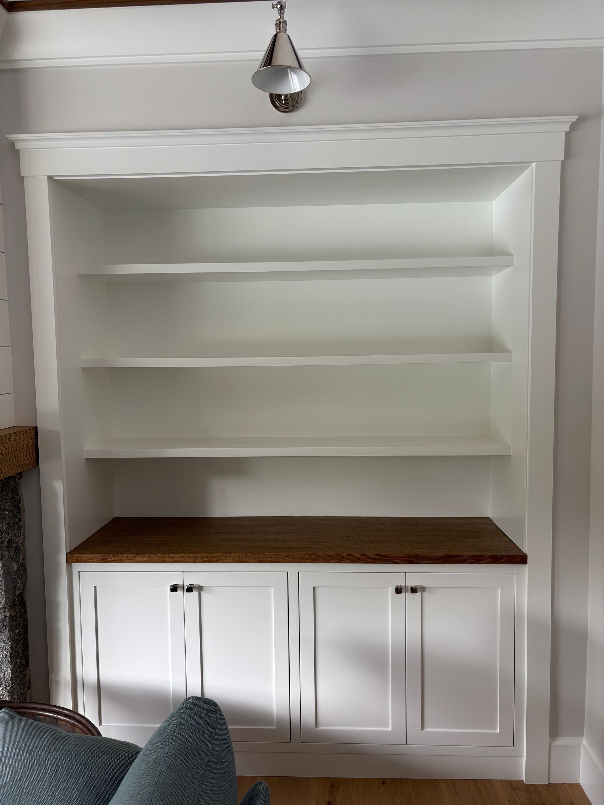 White built-in shelving unit with a wooden countertop and two lower cabinets against a light-colored wall.
