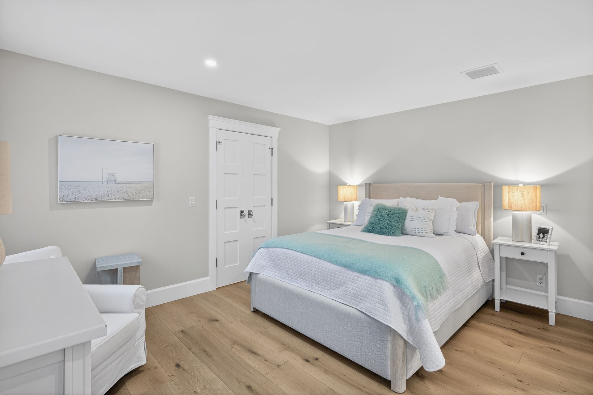 Bedroom with light gray walls, wooden floor, white bed, chair, and nightstand; aqua accents.