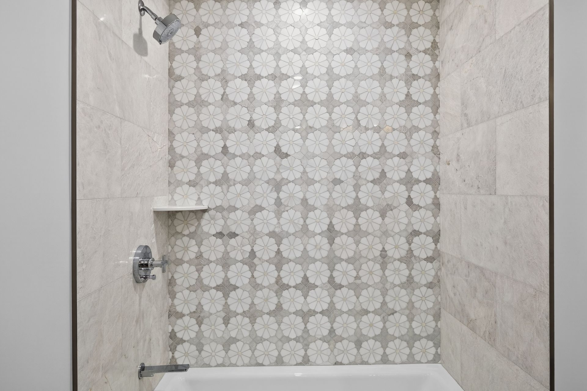 Shower with floral tile accent wall, built-in shelf, silver fixtures, and white tub.
