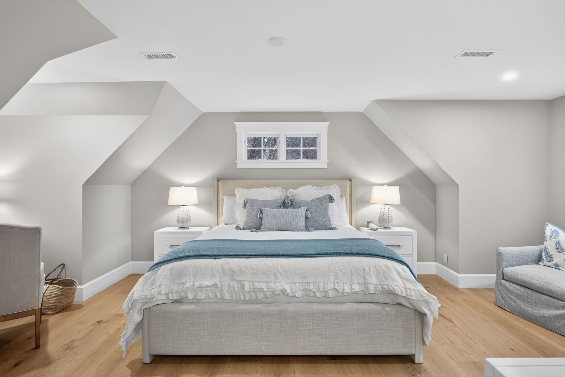 Bedroom with a bed, nightstands, and a small window centered on the wall. Light colors and wood floors.
