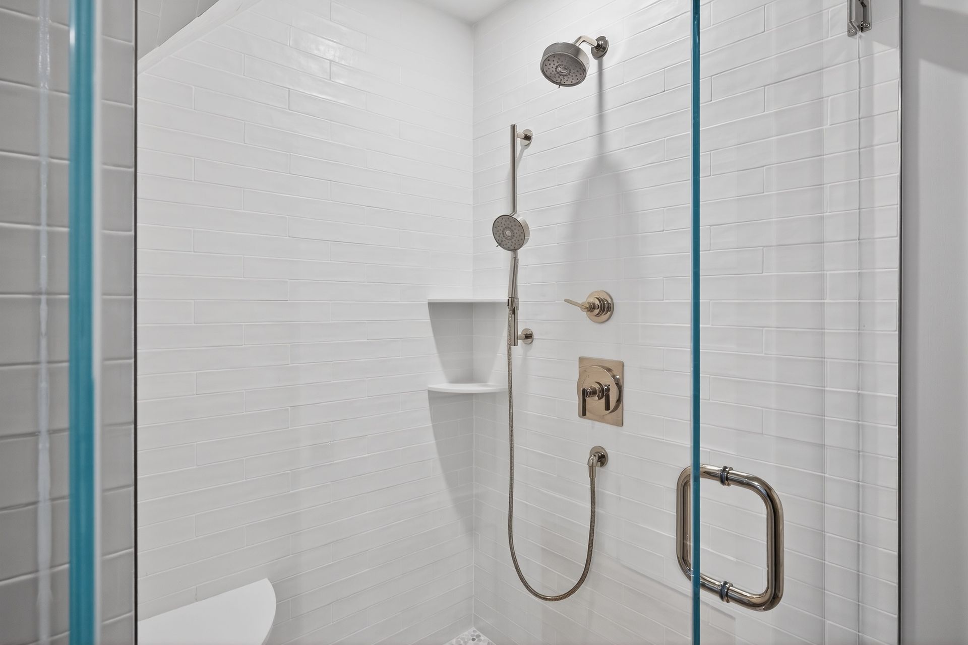 White tiled shower with glass door and silver shower fixtures.