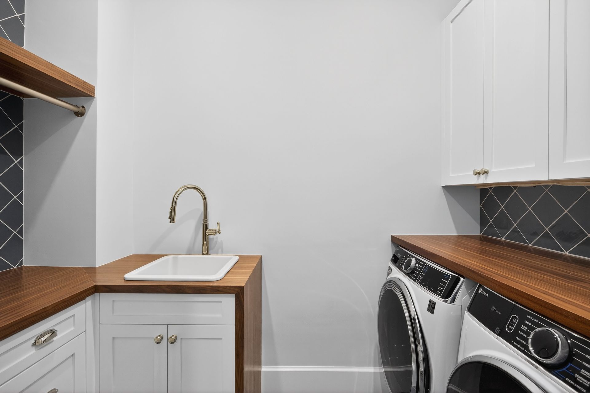Laundry room with white cabinets, dark wood countertops, a sink, and a washer/dryer.