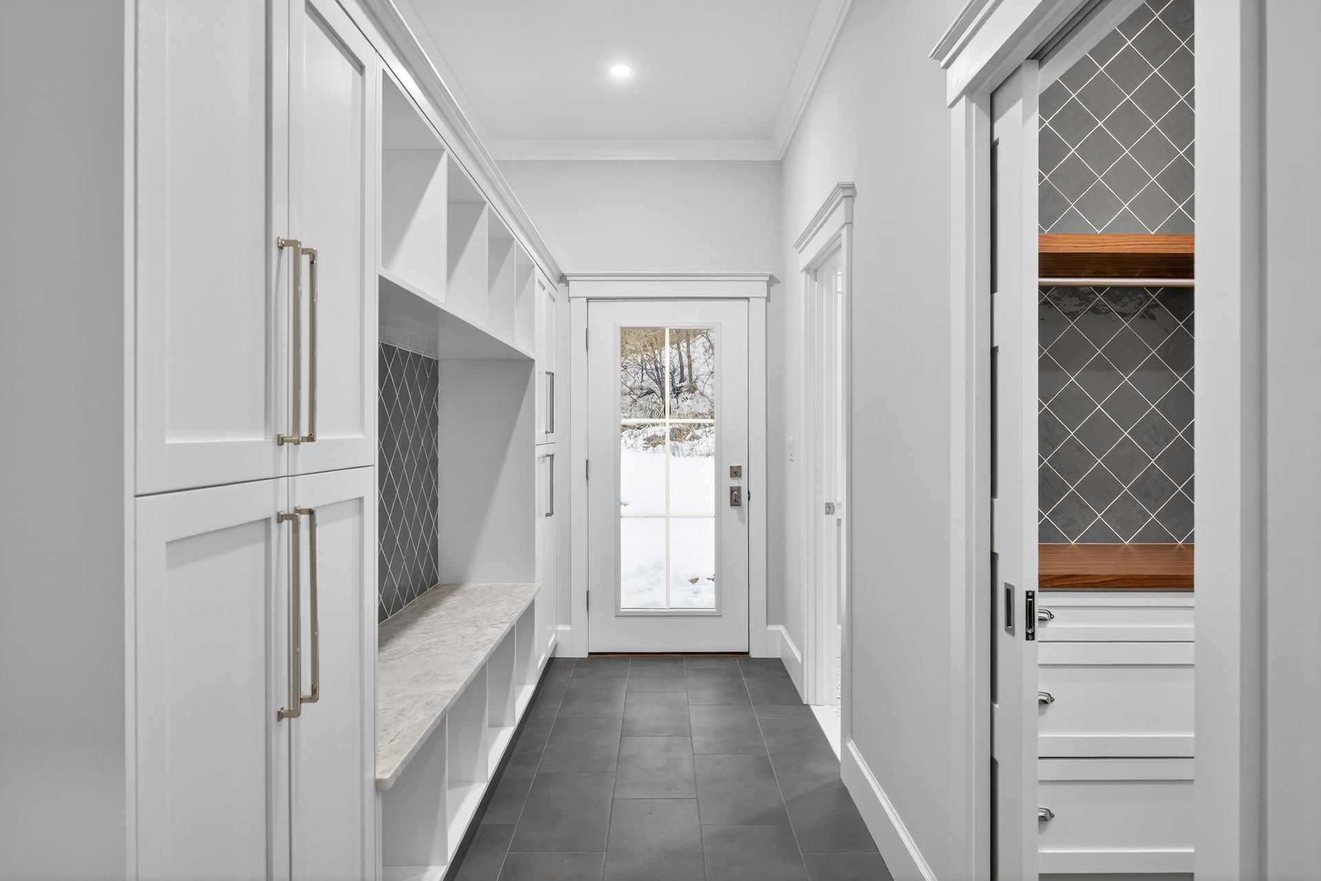 White hallway with built-in storage and a front door. A closet with a lattice glass door is visible.