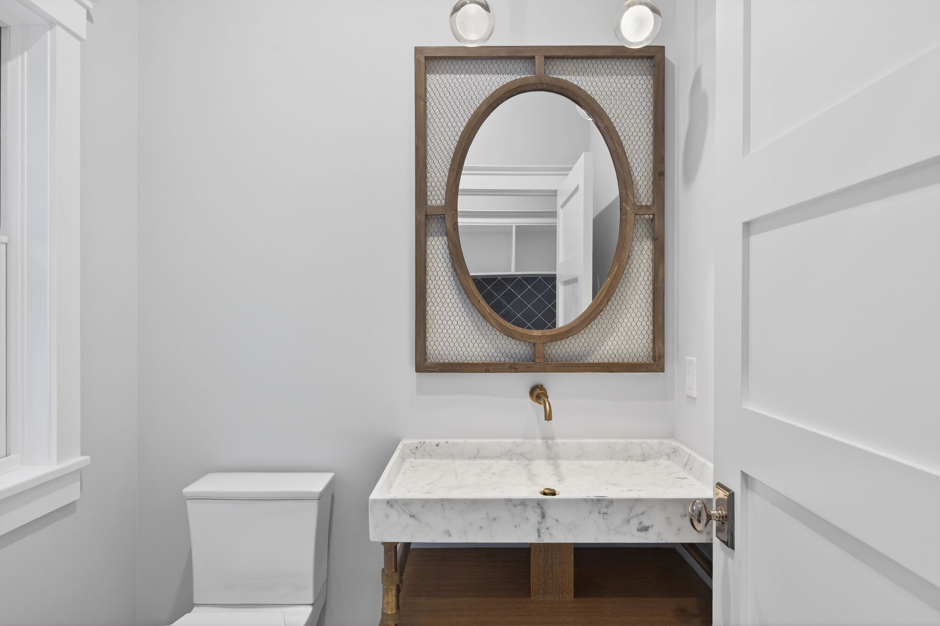 A powder room with a marble sink, oval mirror, and toilet; pale blue walls, white trim.
