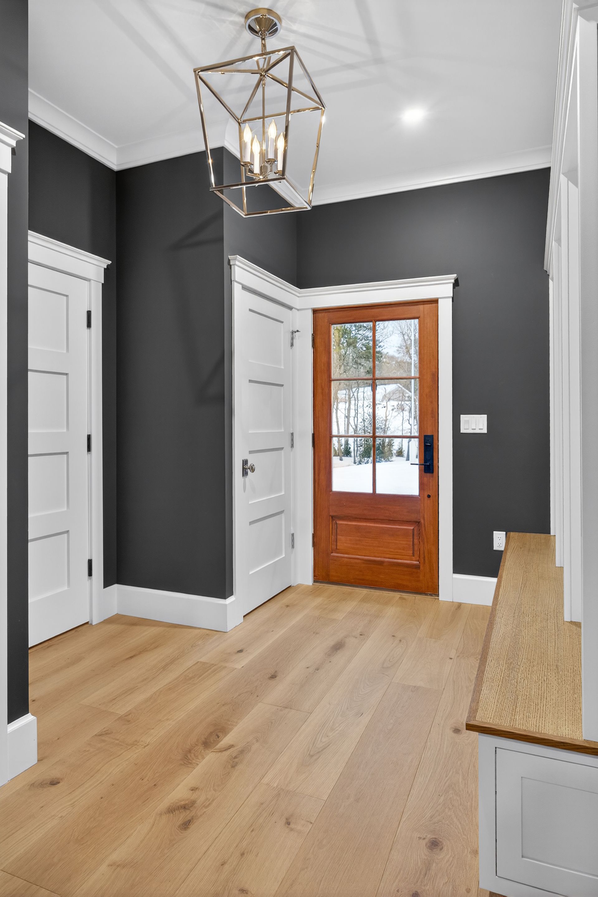Entryway with dark gray walls, white trim, wood door, and light wood flooring.