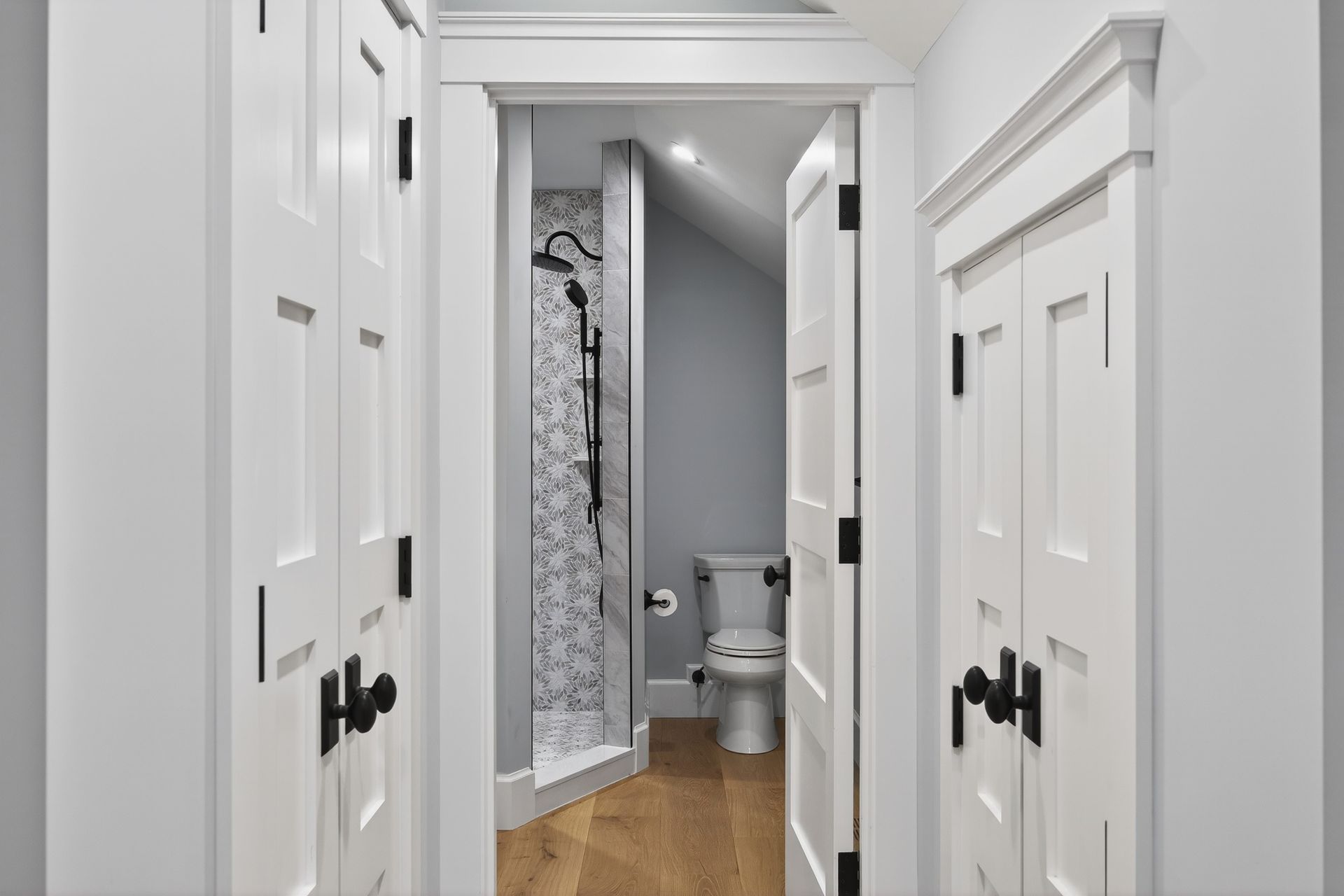 Hallway with white doors, one leading to a small bathroom with a shower and toilet.