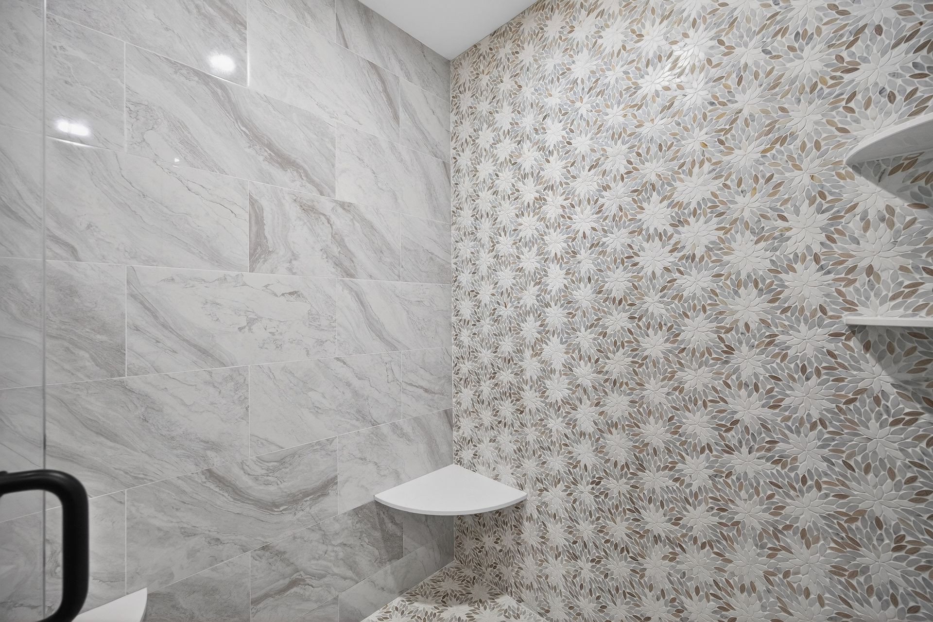 Bathroom corner with patterned mosaic accent wall and marble tile. Two white corner shelves.
