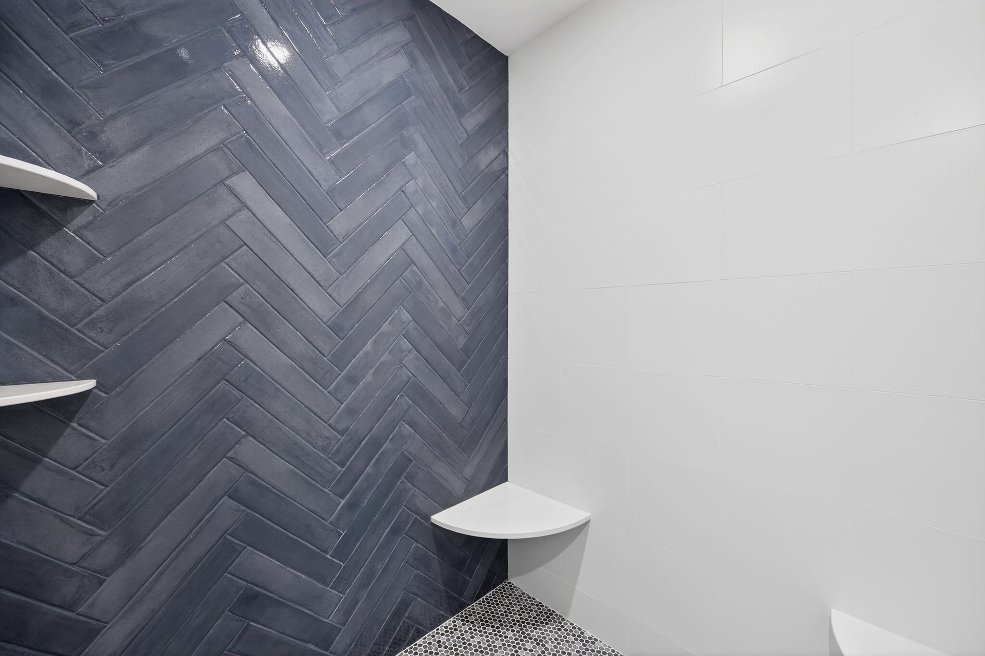 Blue herringbone tiled wall with white corner shelves, next to a white wall.