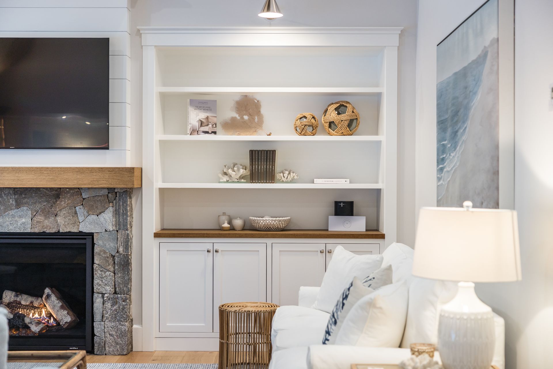 White built-in bookshelf with decorations in a living room, next to a stone fireplace and white sofa.