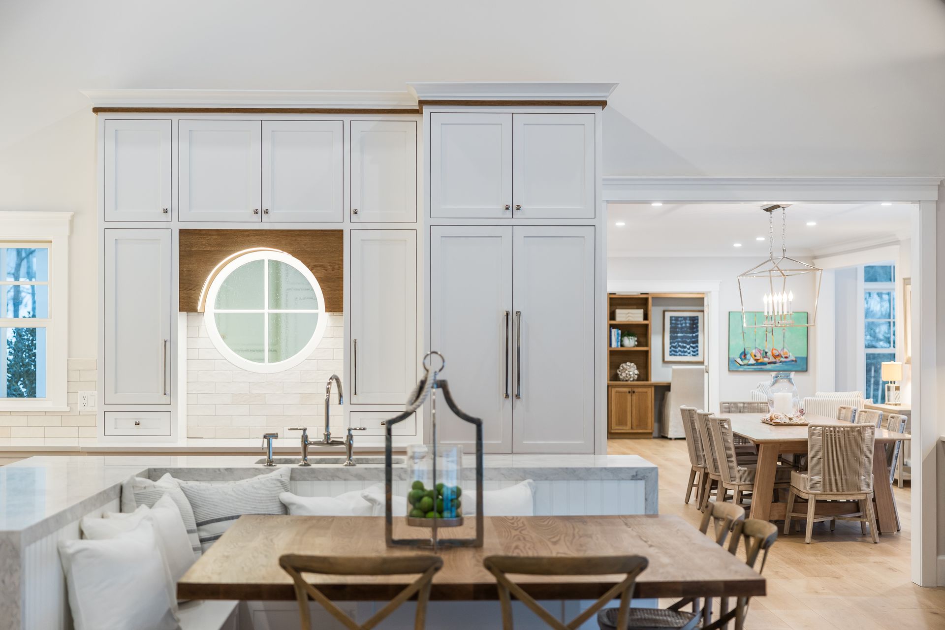 Modern kitchen with white cabinets, round window, and wooden dining table.