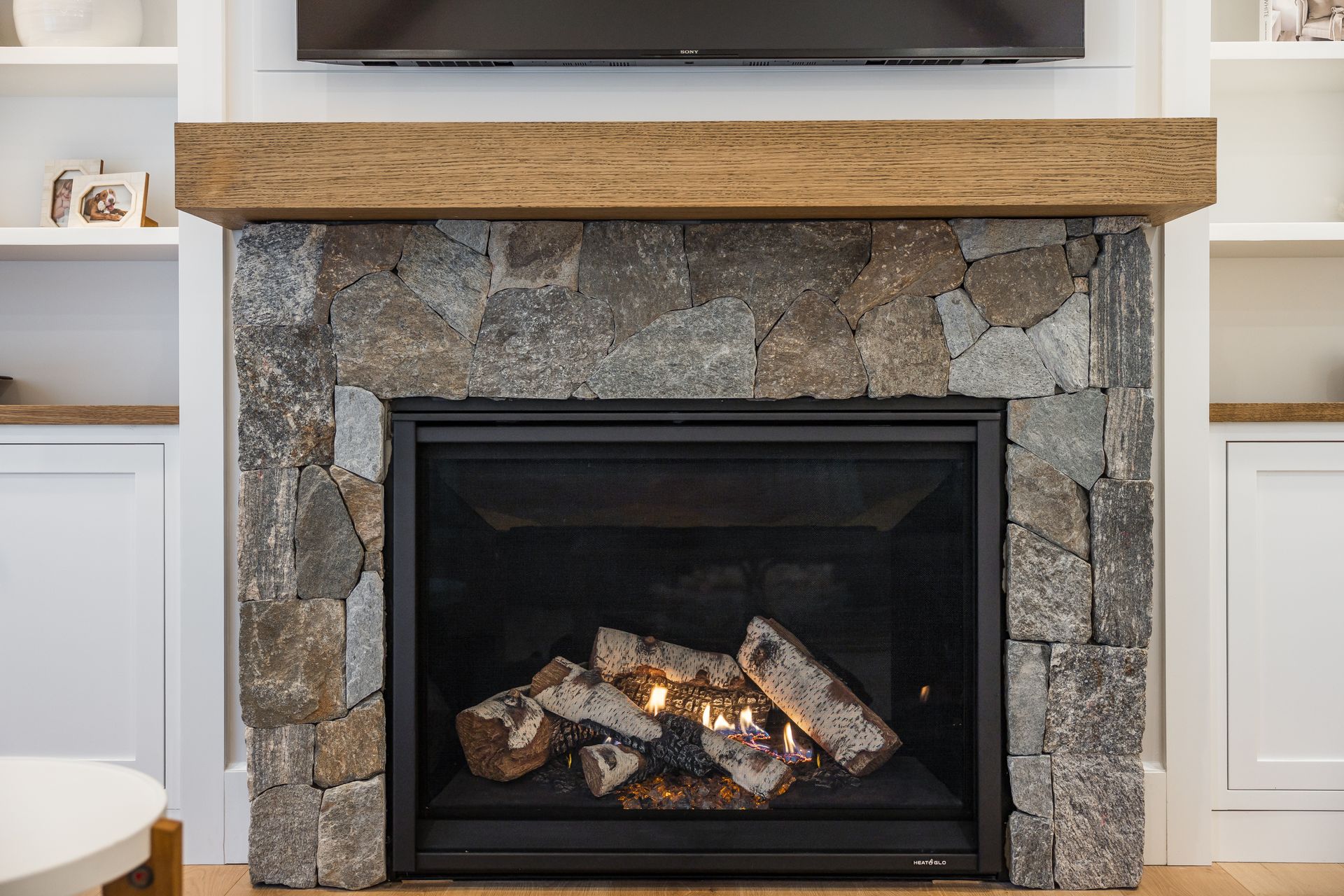 Fireplace with stone facade, wooden mantel, and burning gas logs.