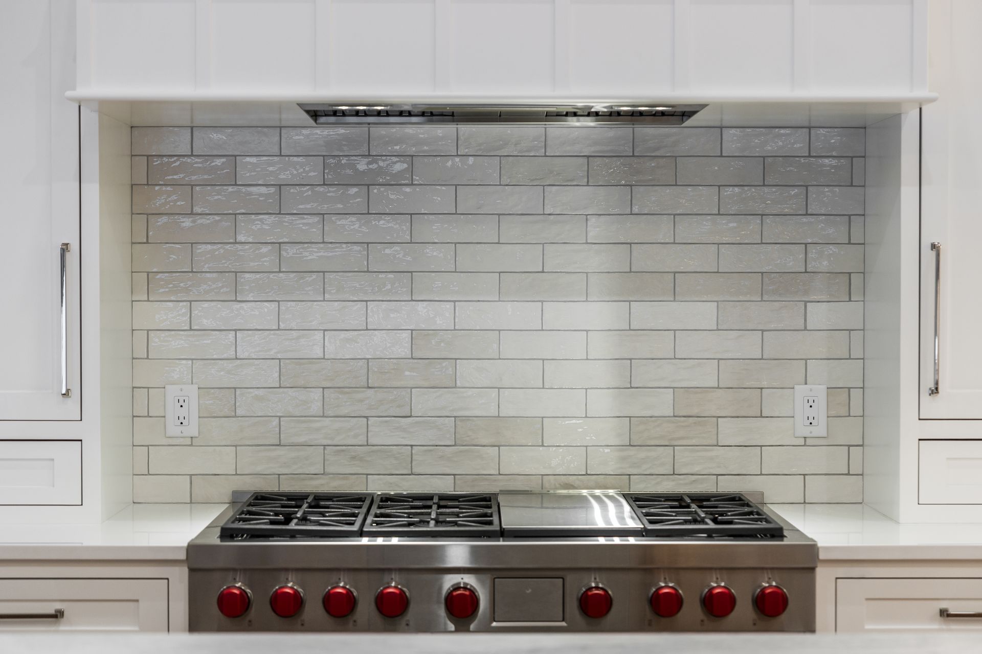 Stainless steel range with red knobs, white cabinets, and brick-style backsplash in a modern kitchen.