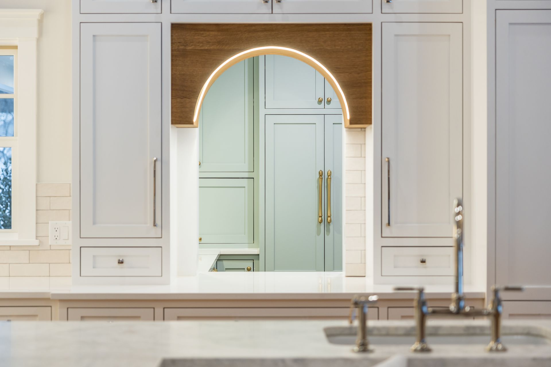 Kitchen with arched wooden detail, illuminated, framed by light gray cabinets and white tiled backsplash.
