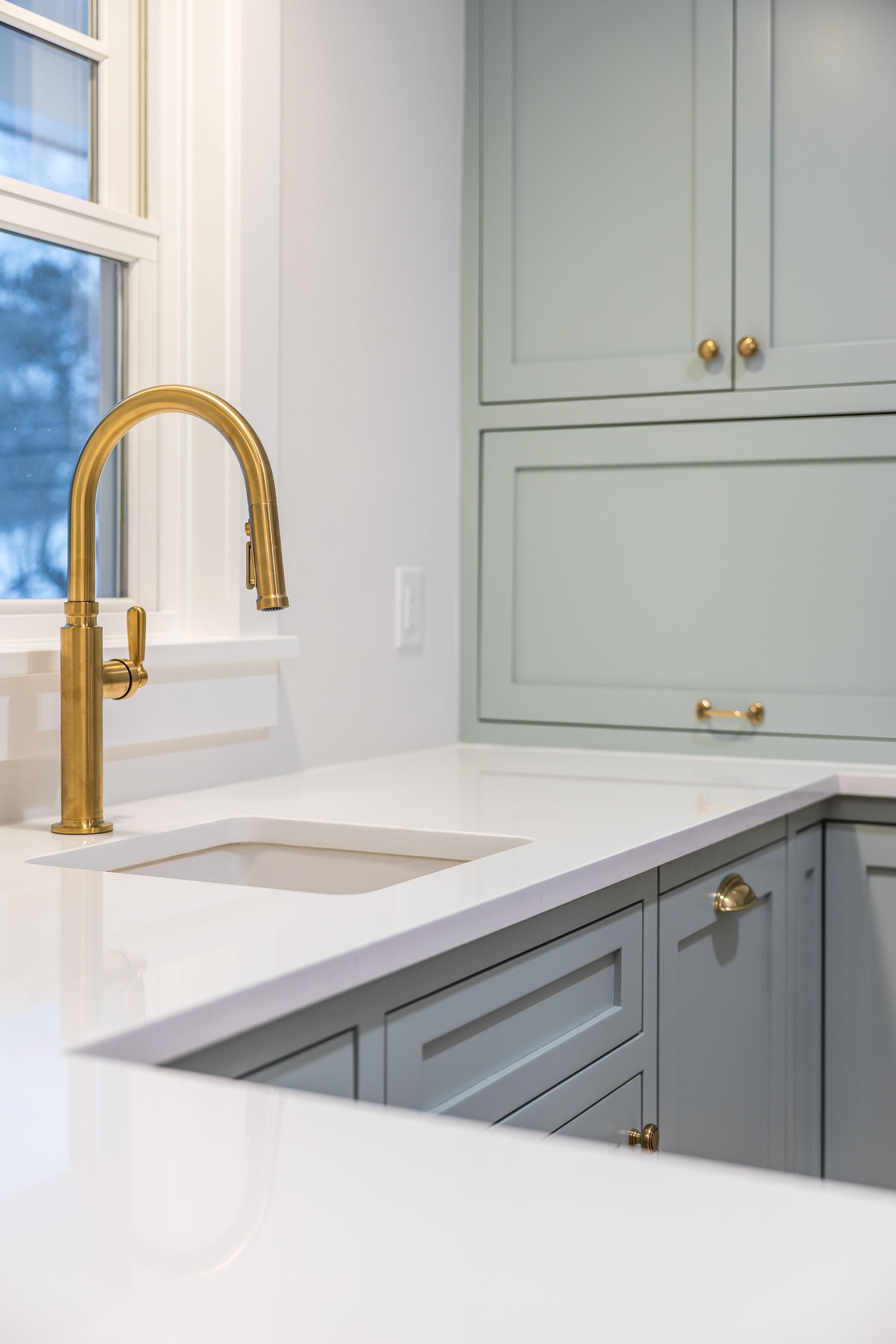 Gold faucet in a light blue kitchen with white countertops and cabinets.