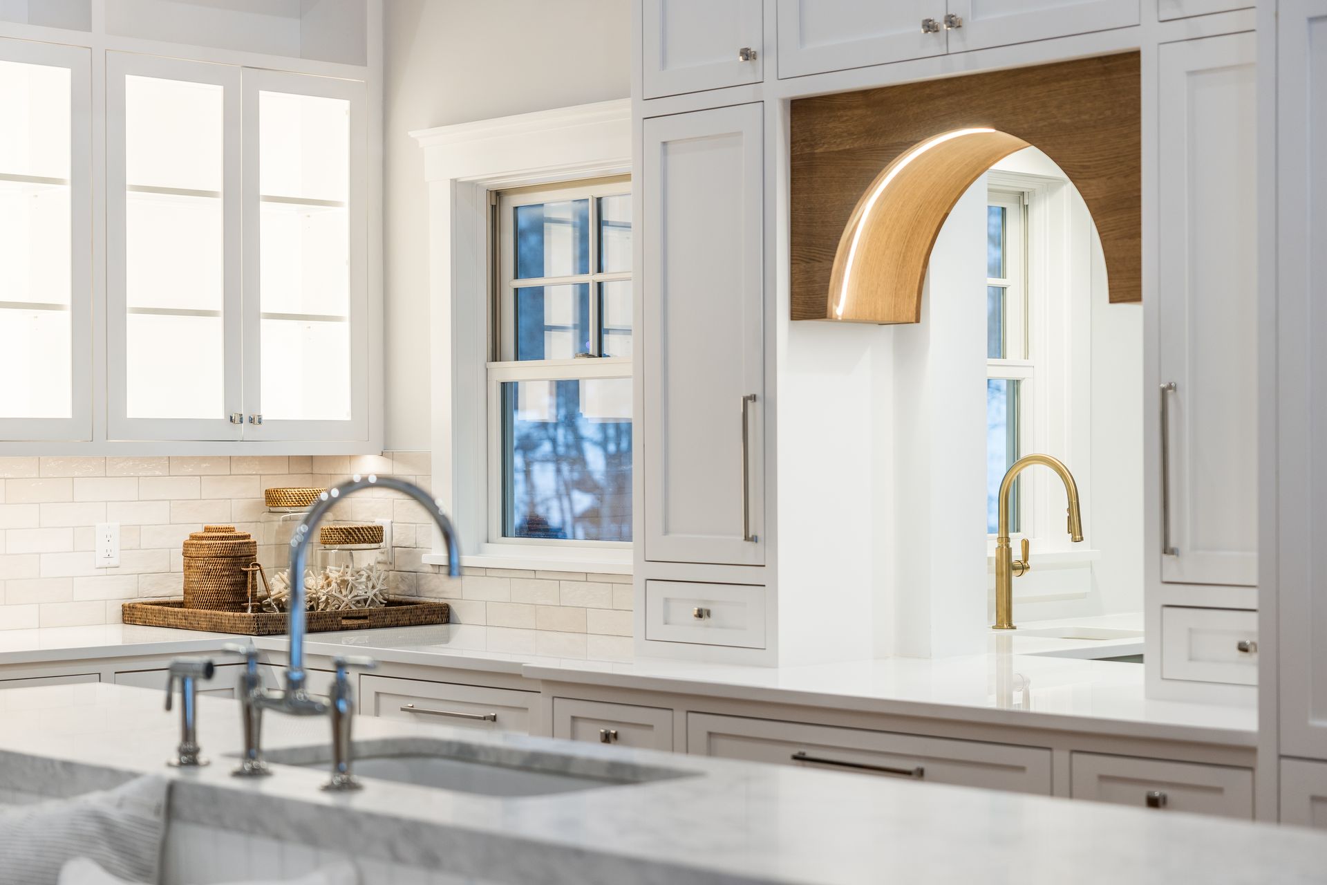 White kitchen with marble countertops, stainless steel and gold fixtures, and an arched design element.